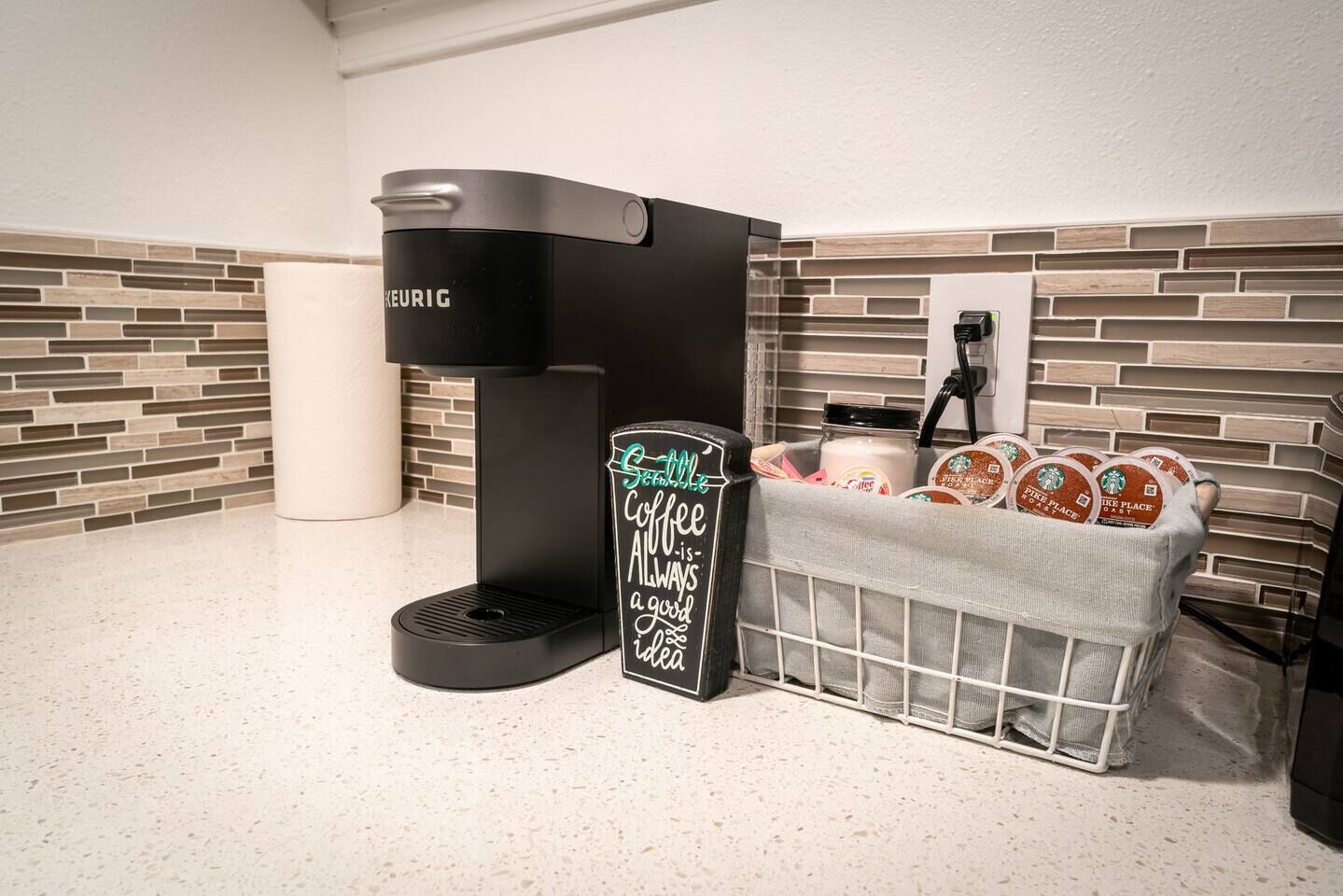 A coffee station with a Keurig coffee maker, a chalkboard sign, and a basket of Starbucks coffee pods.