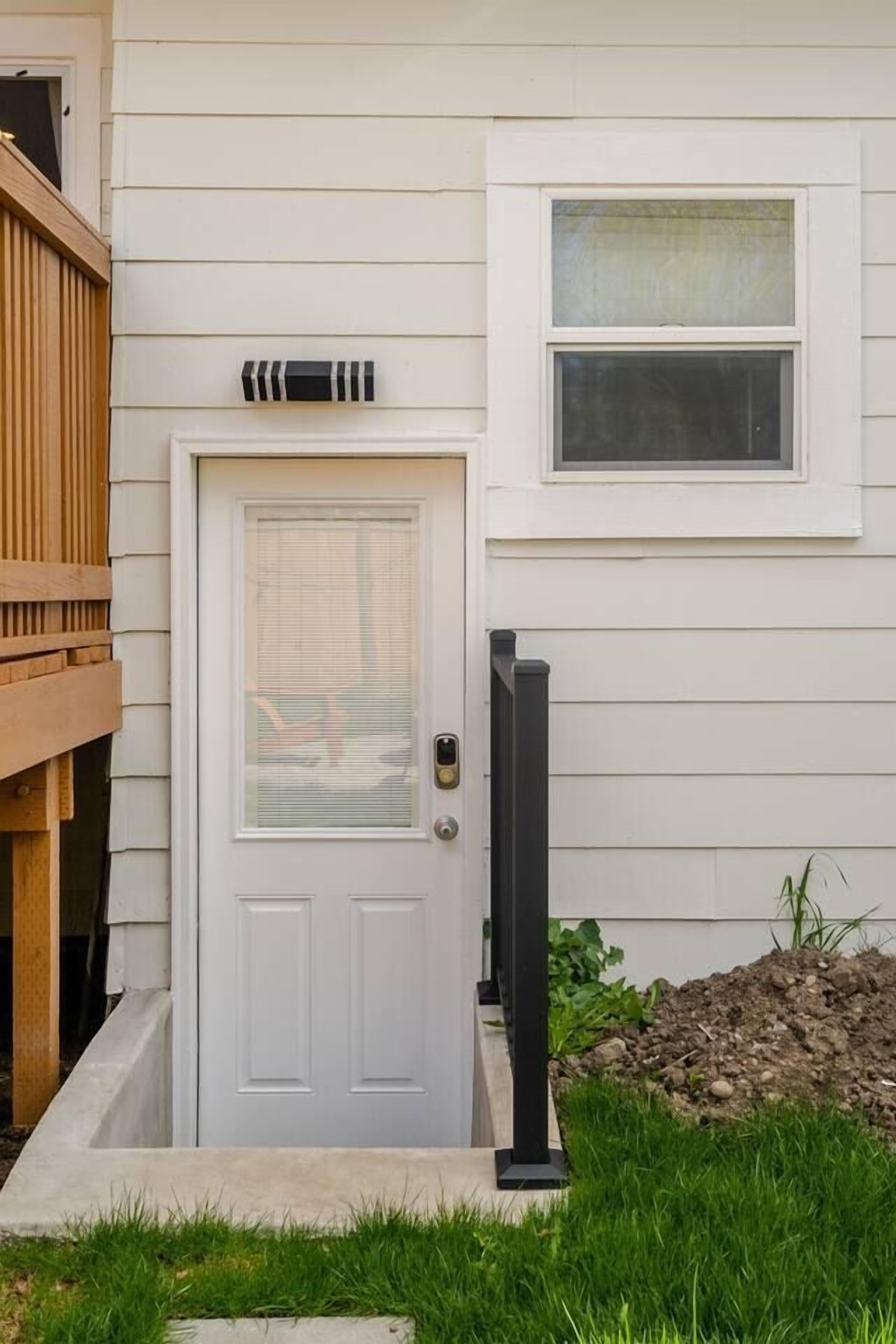 A white door with a window above it, a mailbox, and a small garden area with grass and plants.