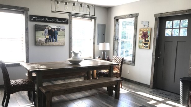 A dining area with a wooden table, bench, and wicker chairs. There is a wall-mounted light fixture above the table.