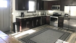 A modern kitchen with dark cabinets, stainless steel appliances, a marble countertop, and a patterned rug.