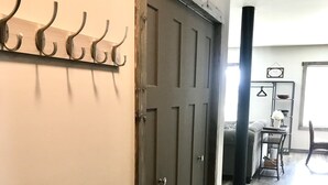 A hallway with a wooden floor, a dark door, and a coat rack with hooks.