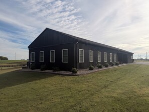 A long, dark-colored building with multiple windows, a sloped roof, and a grassy area in front.