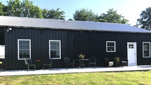 A black metal building with a corrugated roof, large windows, and a door.