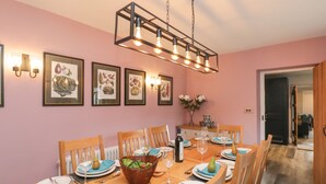 Ein Esszimmer mit Holztisch, gedeckt für sechs Personen, Bilderrahmen an der Wand und einer Hängelampe darüber.