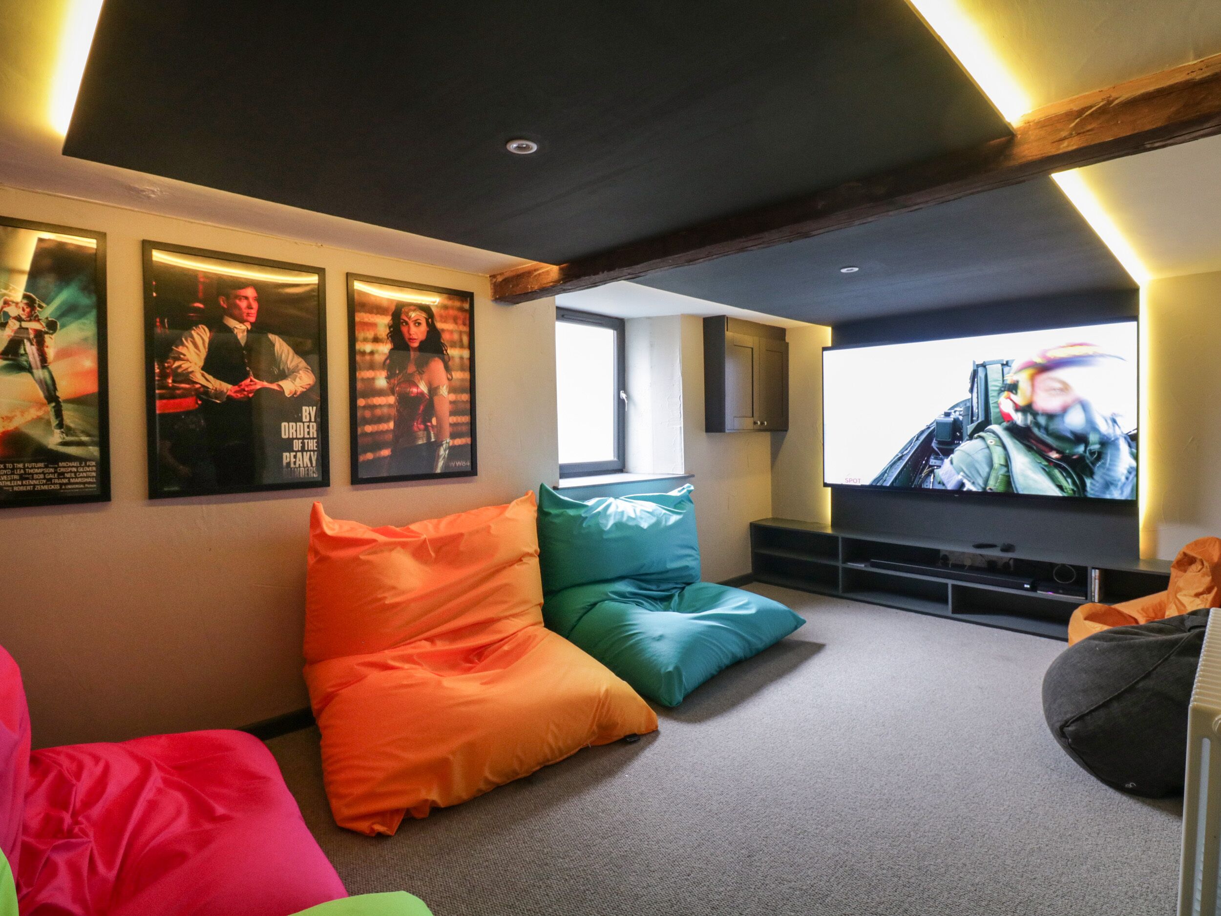 Ein modernes Wohnzimmer mit großem Flachbildfernseher, bunten Kissen und gerahmten Filmplakaten an der Wand.