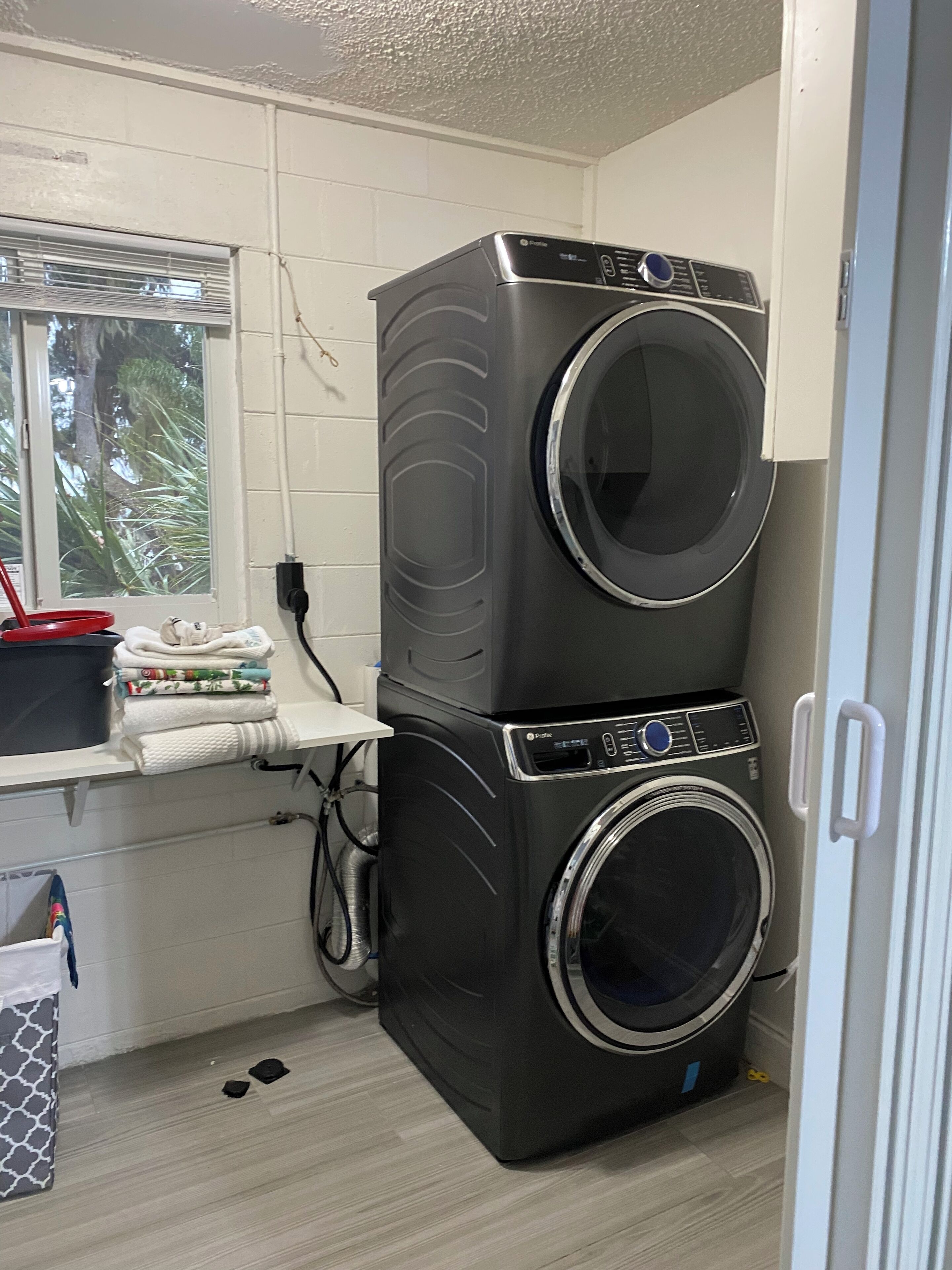 A laundry area with stacked washers and dryers, a window with a view of palm trees, and a countertop with folded towels.