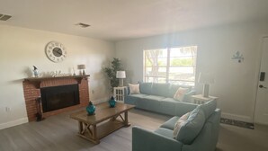 A spacious living room with a fireplace, a blue sofa, a coffee table, and a large window. - COUNTRYSIDE VACATION BY THE LAKE HOUSE CENTRAL FLORIDA (Frostproof)
