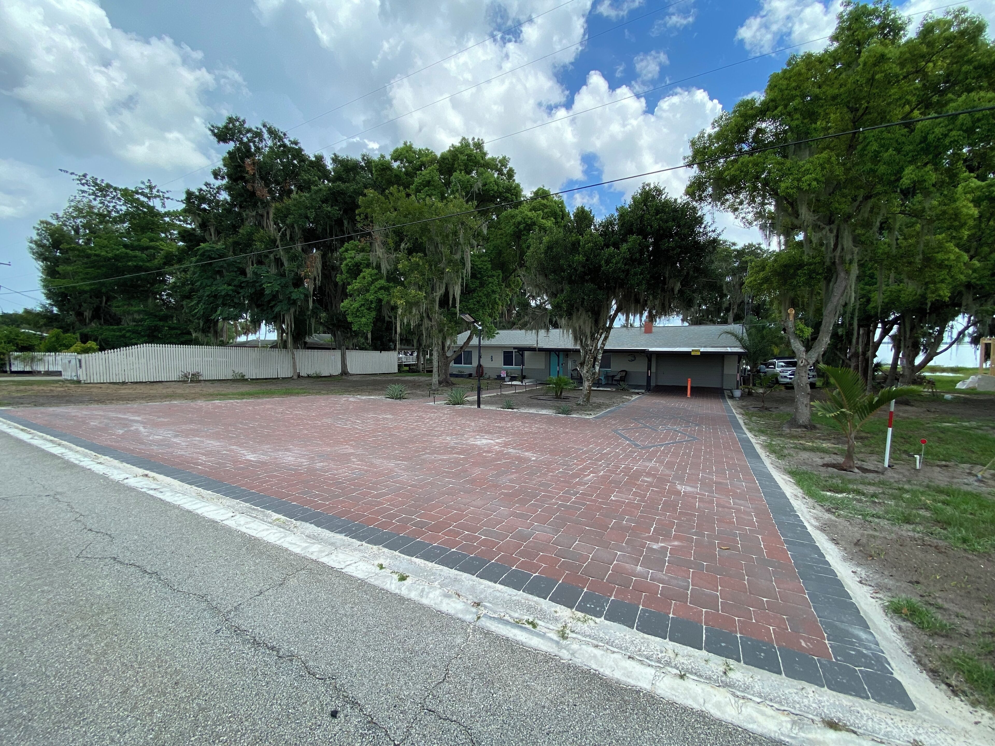Un camino pavimentado que conduce a un edificio con techo gris y una valla blanca al fondo.