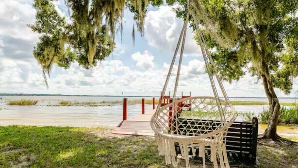 A hammock under a tree by a body of water with a wooden dock in the background. - COUNTRYSIDE VACATION BY THE LAKE HOUSE CENTRAL FLORIDA (Frostproof)