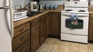 A kitchen with wooden cabinets, a white refrigerator, a stove, and a window with lace curtains. - Horseshoe Cottage:  SKI, FISH, HIKE & BIKE: Paradise near all things outdoor! (Parsons)