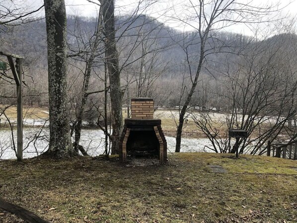 An outdoor brick fireplace surrounded by trees and a body of water. - Horseshoe Cottage: SKI, FISH, HIKE & BIKE: Paradise near all things outdoor! (Parsons)