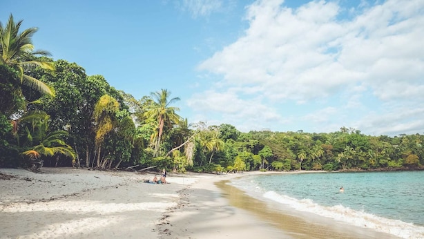 A beach with clear turquoise water, sandy shore, and lush green vegetation. - VAL HOTEL (Quepos)