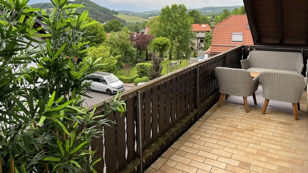 A balcony with wicker furniture, a view of a green landscape, and a parked car.