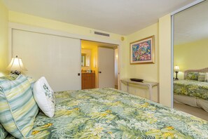 A hotel room with a bed, a nightstand, a lamp, a painting, and a door leading to another room.