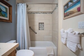 A bathroom with a shower, toilet, and bathtub. There is a towel rack with towels, a framed picture on the wall, and a small decorative tile feature.