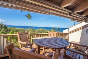 A wooden deck with a round table and chairs, overlooking a scenic ocean view.