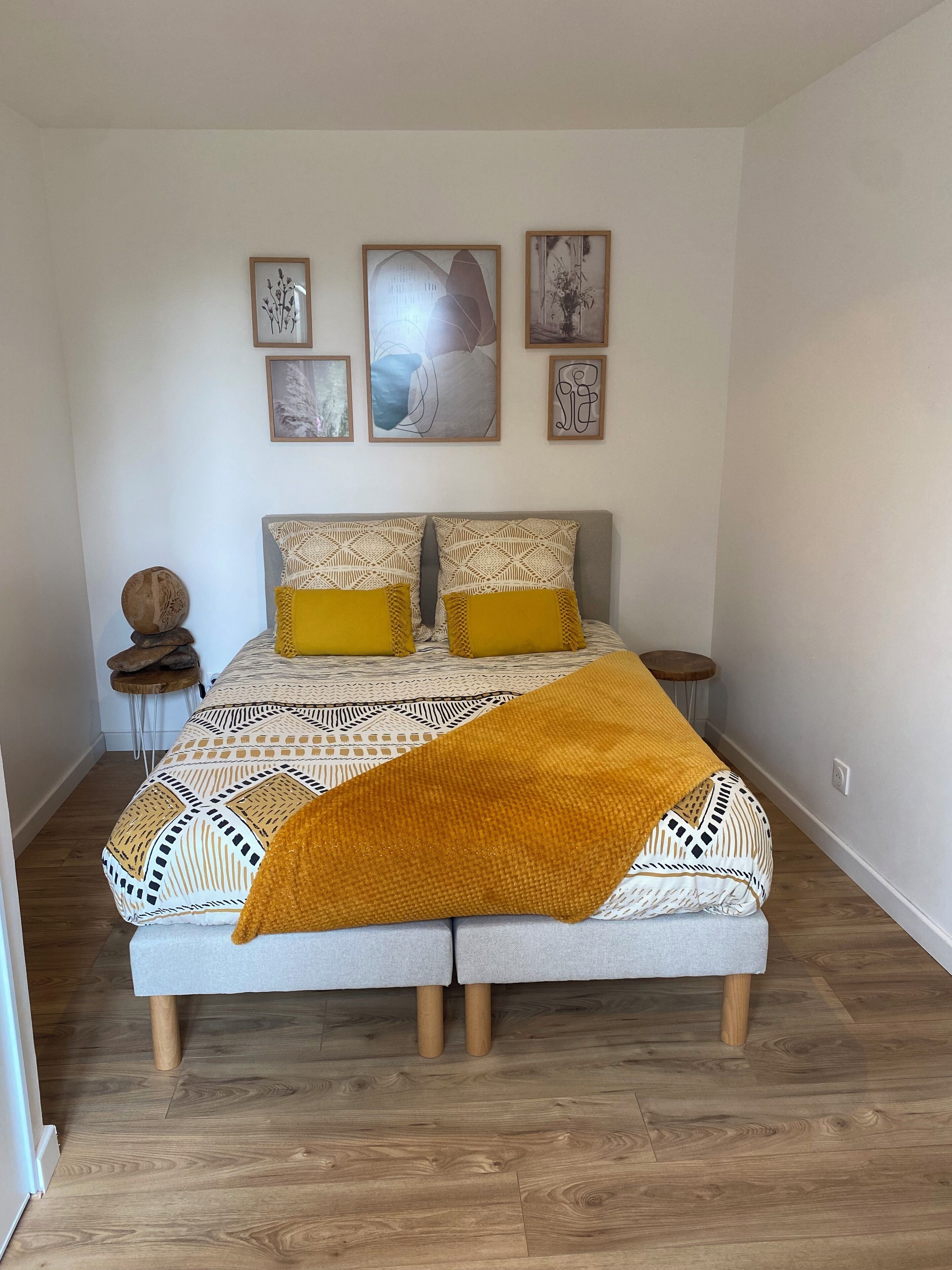 A bedroom with a bed, two nightstands, a round decorative item, and four framed pictures on the wall.
