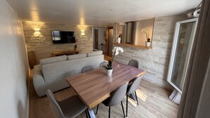 A modern dining area with a wooden table and chairs, a grey sofa, and a stone wall with a flat-screen TV.