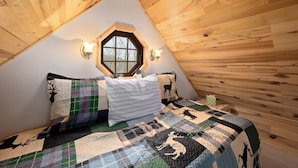 Une chambre avec un plafond en pente, une fenêtre hexagonale et une couvre-lit matelassé.