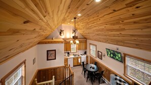 L’intérieur chaleureux d’un chalet avec un plafond en bois, un coin repas, une cuisine et un escalier menant à un étage supérieur.