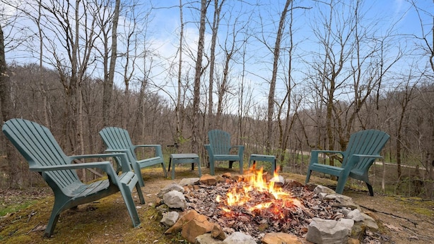 Un feu de camp entouré de fauteuils Adirondack, dans une zone boisée.