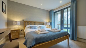 A bedroom with a wooden bed, bedside tables, a desk, and a view of the outdoors. - Riverside Park 3 (Keswick)