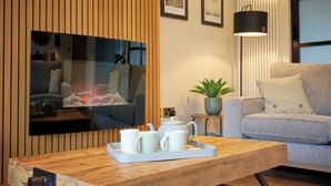 A modern living room with a wooden TV stand, a grey sofa, a small side table with a plant, and a tray with teapots and cups. - Riverside Park 3 (Keswick)