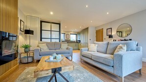 A modern living room with two grey sofas, a wooden coffee table, and a large mirror. - Riverside Park 3 (Keswick)