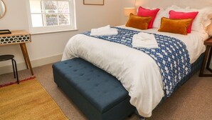 Un lit bien fait, avec une couette à motifs, une table de chevet avec une lampe et une fenêtre donnant sur l’extérieur.