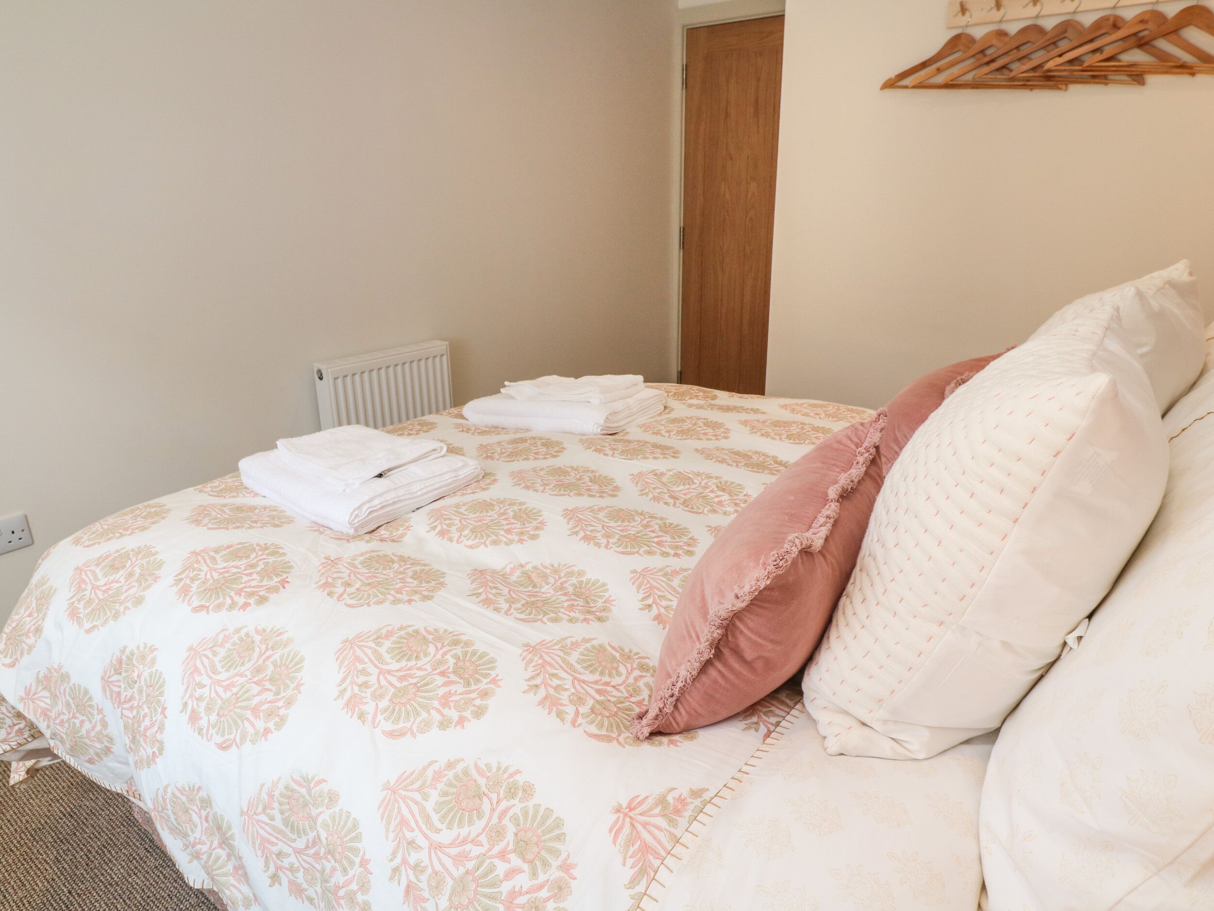 Un lit bien fait, recouvert d’une couvre-lit à motifs floraux, avec un oreiller rose et un oreiller blanc.