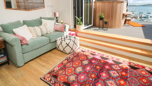 Un salon avec un canapé vert, un tapis à motifs et une vue sur un port de plaisance.