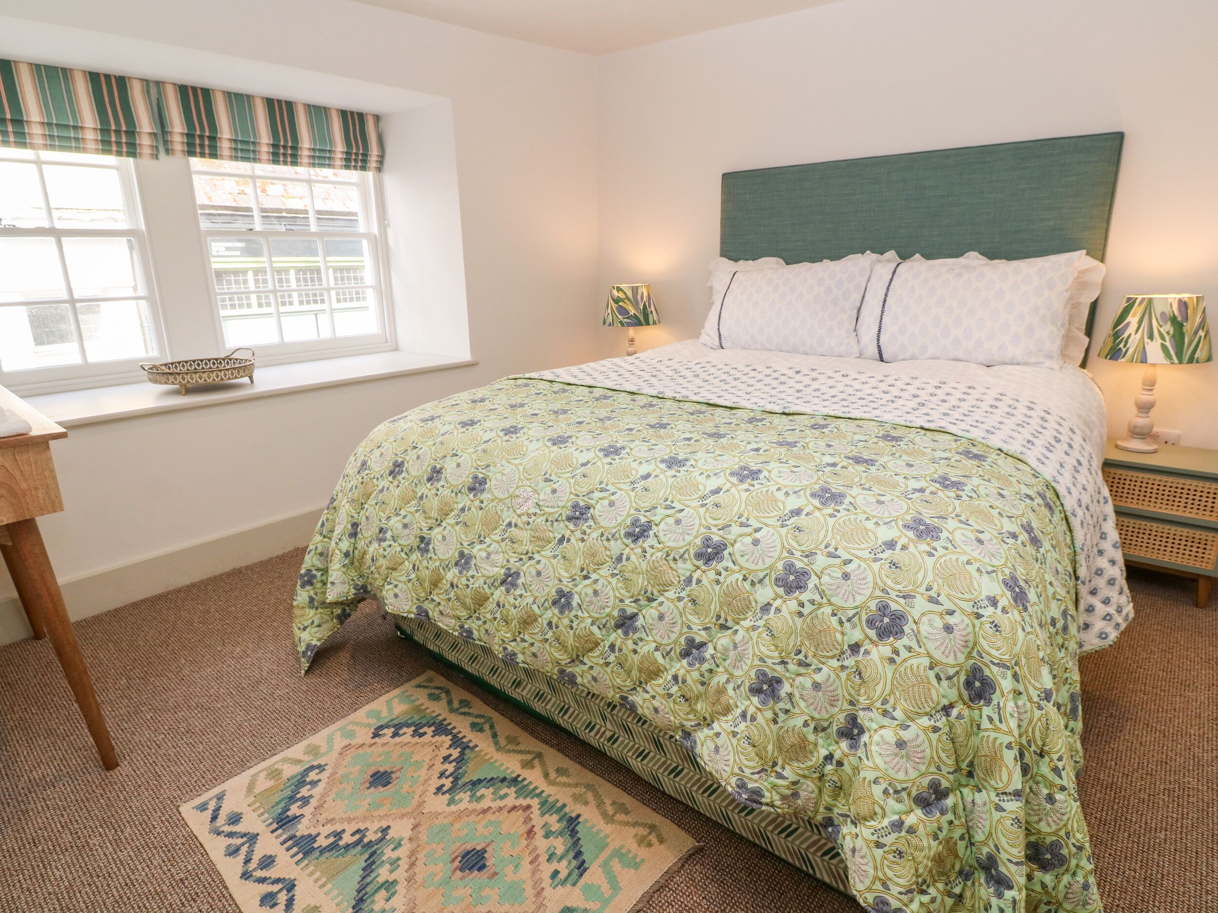A bedroom with a bed, a window with curtains, a bedside table, and a rug.