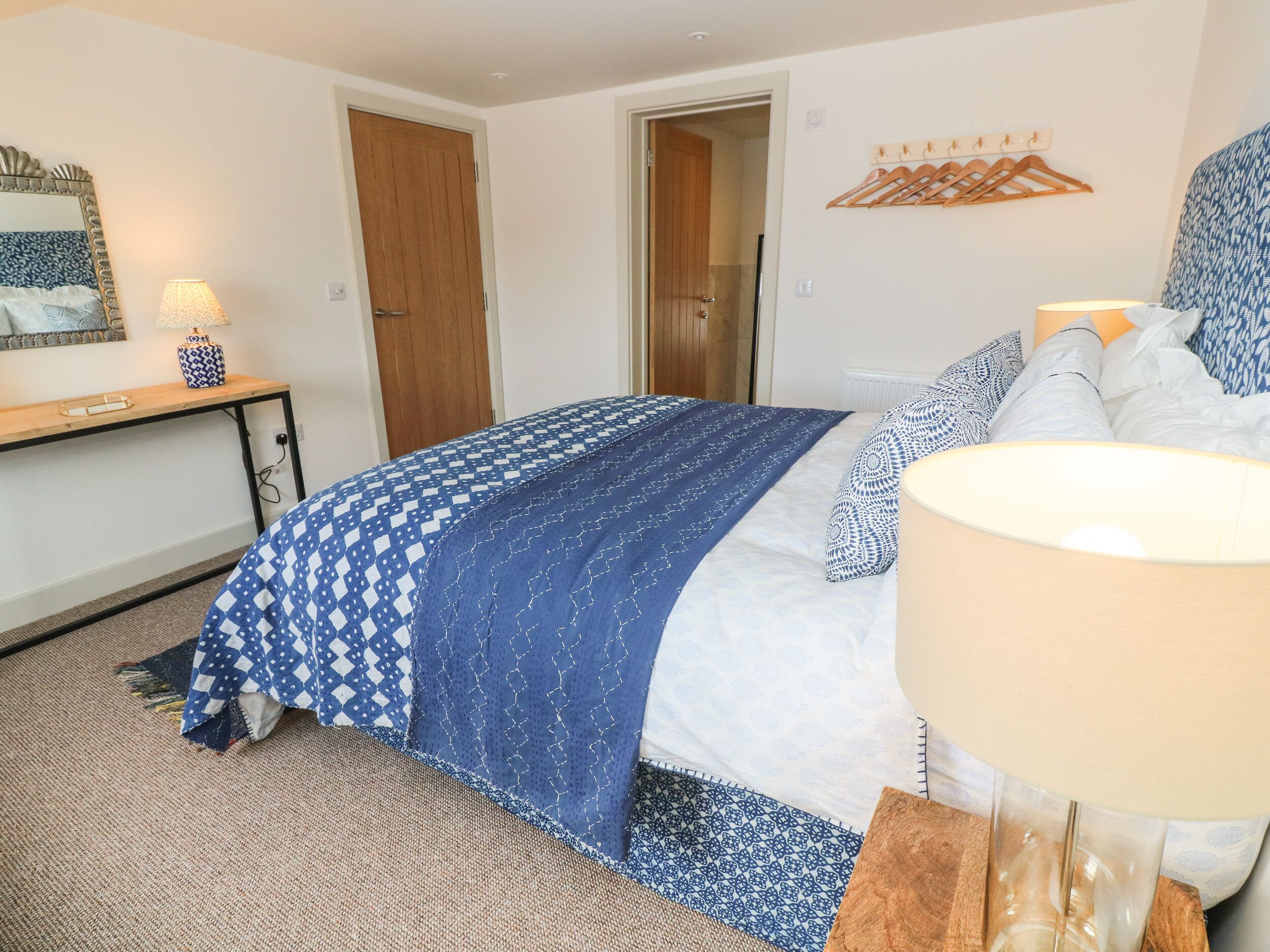 A bedroom with a bed, bedside table, lamp, and a door leading to another room.