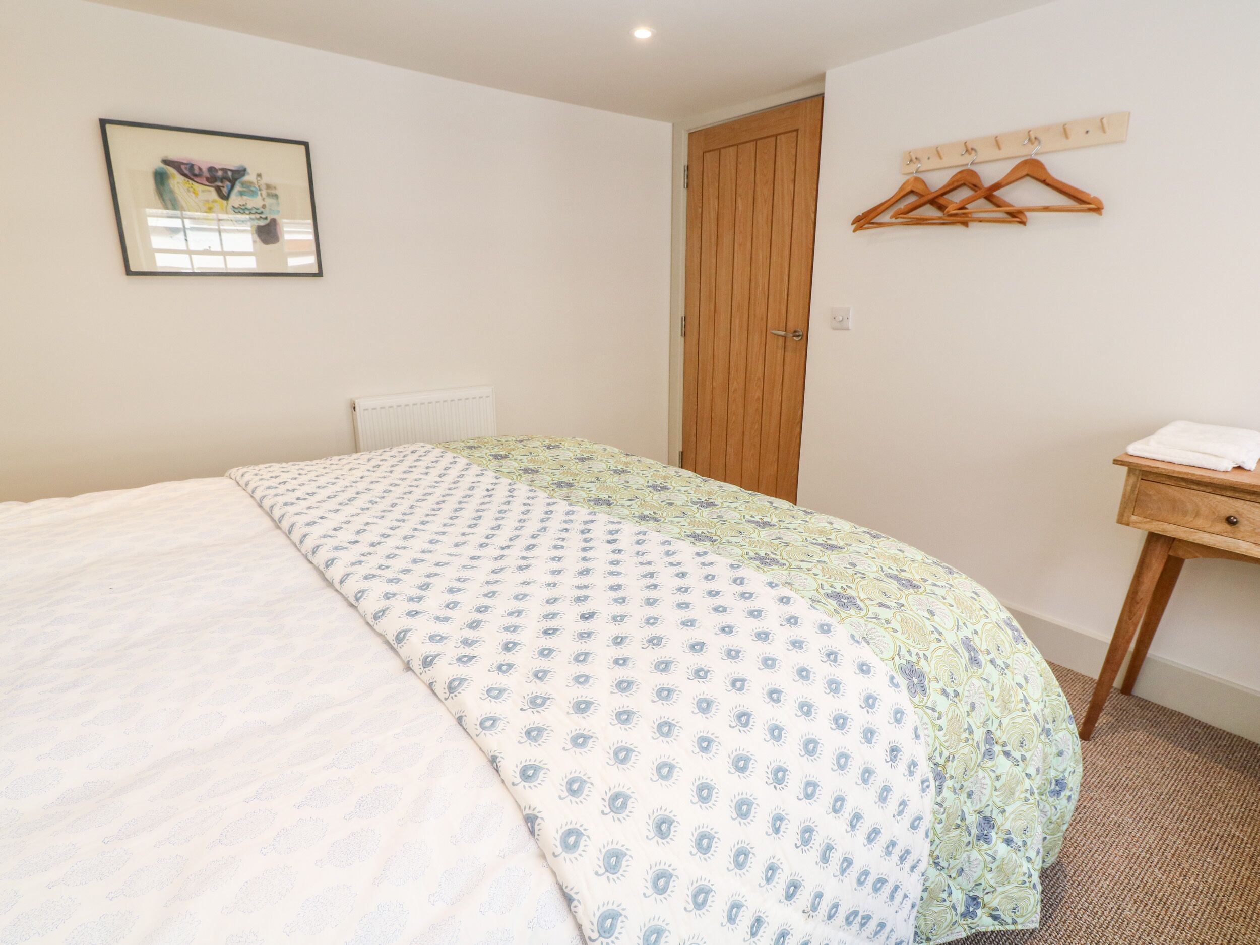 A bedroom with a bed, a wooden door, a coat rack, and a small wooden table with a towel.