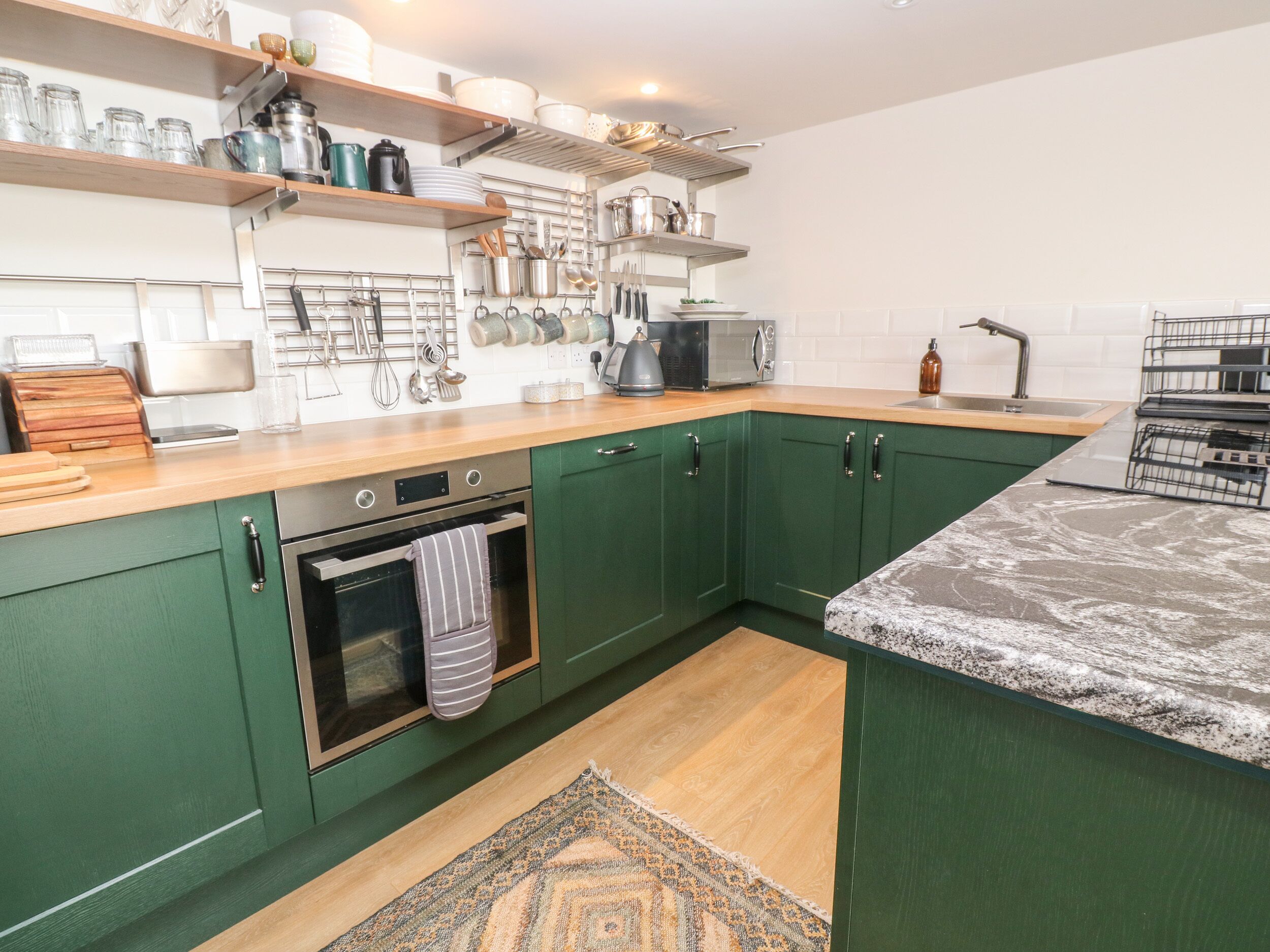A kitchen with green cabinets, a wooden countertop, a built-in oven, and various kitchen utensils and appliances.
