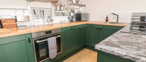 A kitchen with green cabinets, a wooden countertop, a built-in oven, and various kitchen utensils and appliances.