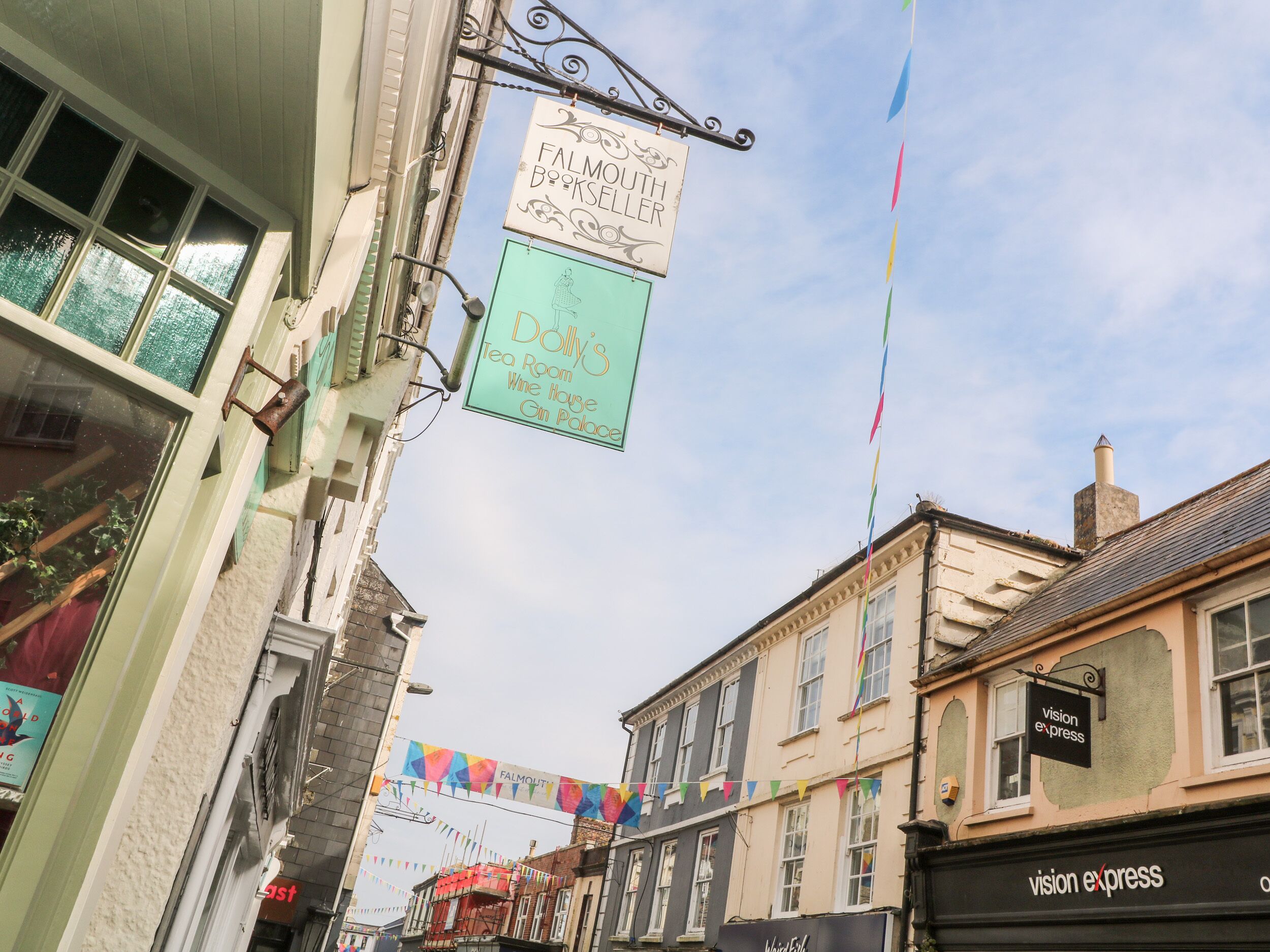 A street view with a building featuring a sign for 'Falmouth Book Seller' and 'Dolly's Tea Room, Wine House, Gin Palace'.