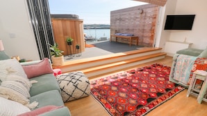 A modern living room with a green sofa, a red patterned rug, and a wooden bench by a large window overlooking a body of water. - 16 Arwenack Street (Falmouth)