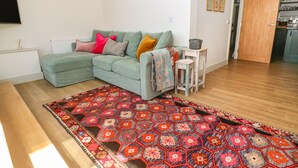 Un salon avec un canapé d’angle, un tapis à motifs et une petite table d’appoint.
