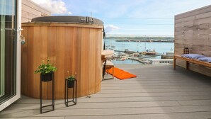 Une terrasse en bois avec un jacuzzi, des plantes en pot et une vue sur un port de plaisance.