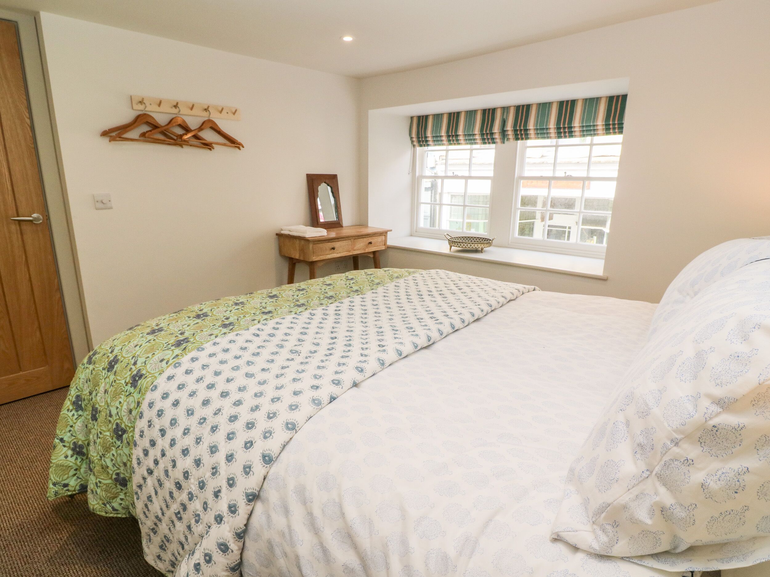 A bedroom with a bed, a dresser, a mirror, and a window with a view.