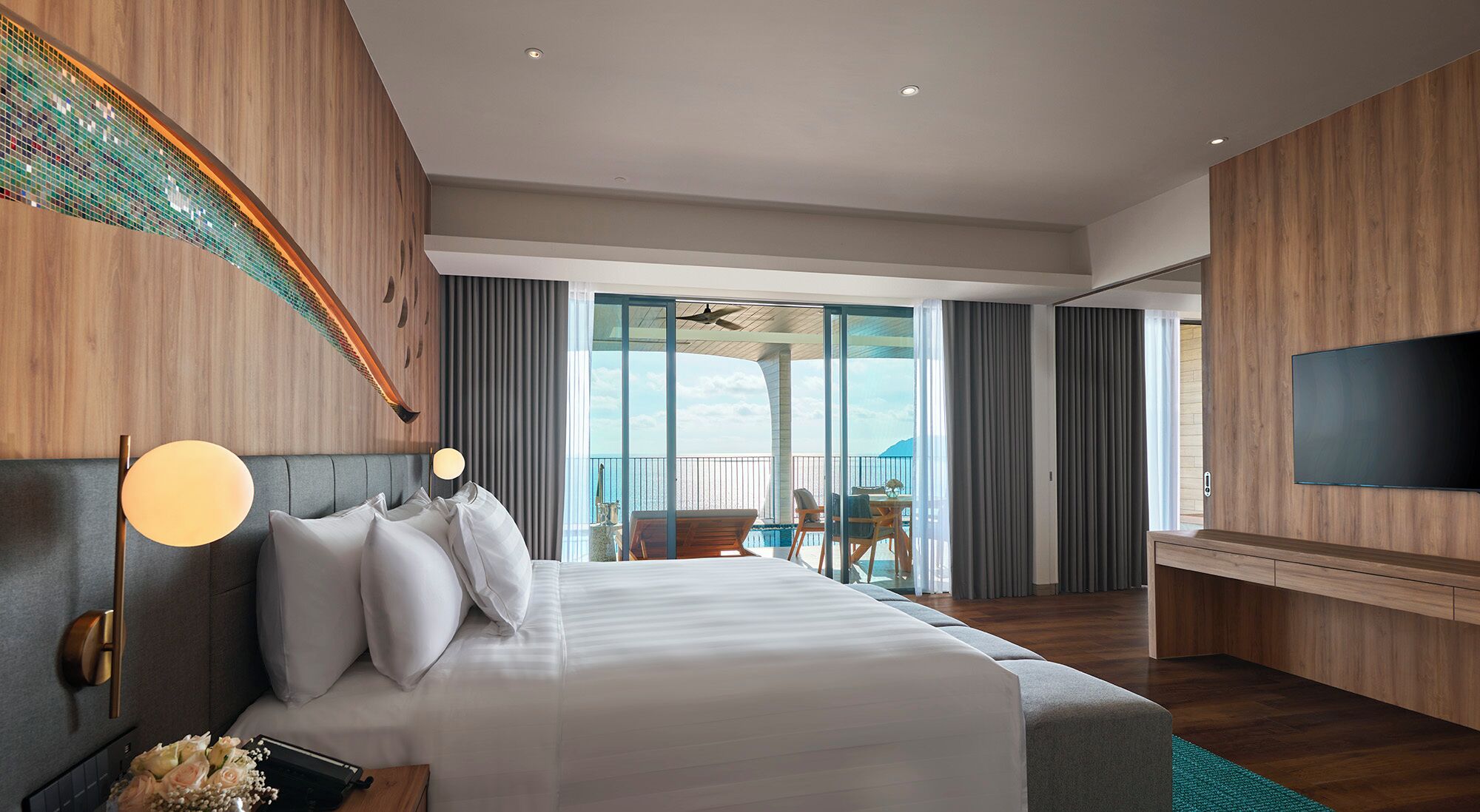 Quarto de hotel com uma cama grande, televisão de tela plana, varanda com vista e ventilador de teto.