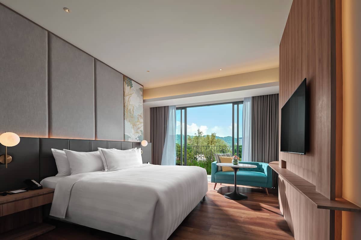 Une chambre d’hôtel moderne dotée d’un grand lit, d’un bureau, d’une chaise, d’une télévision et d’un balcon offrant une vue sur l’extérieur.