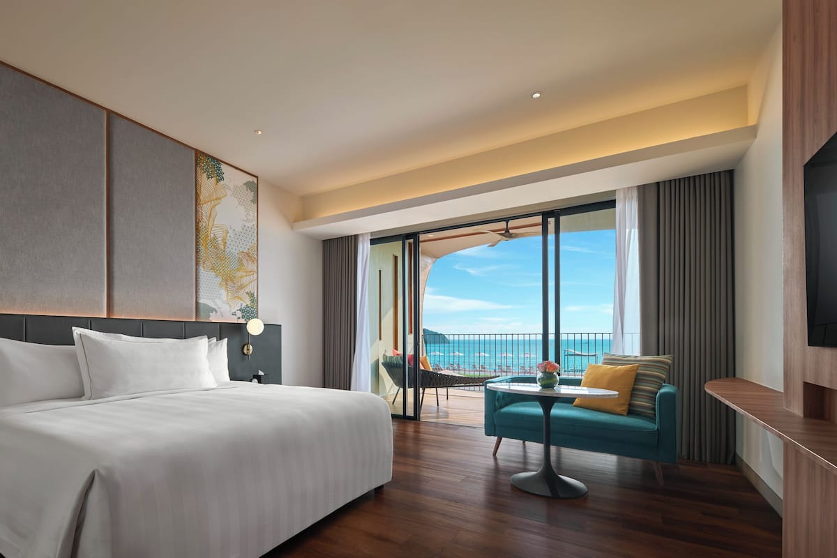 Une chambre d’hôtel moderne avec un grand lit, un balcon offrant une belle vue, une petite table et un téléviseur.