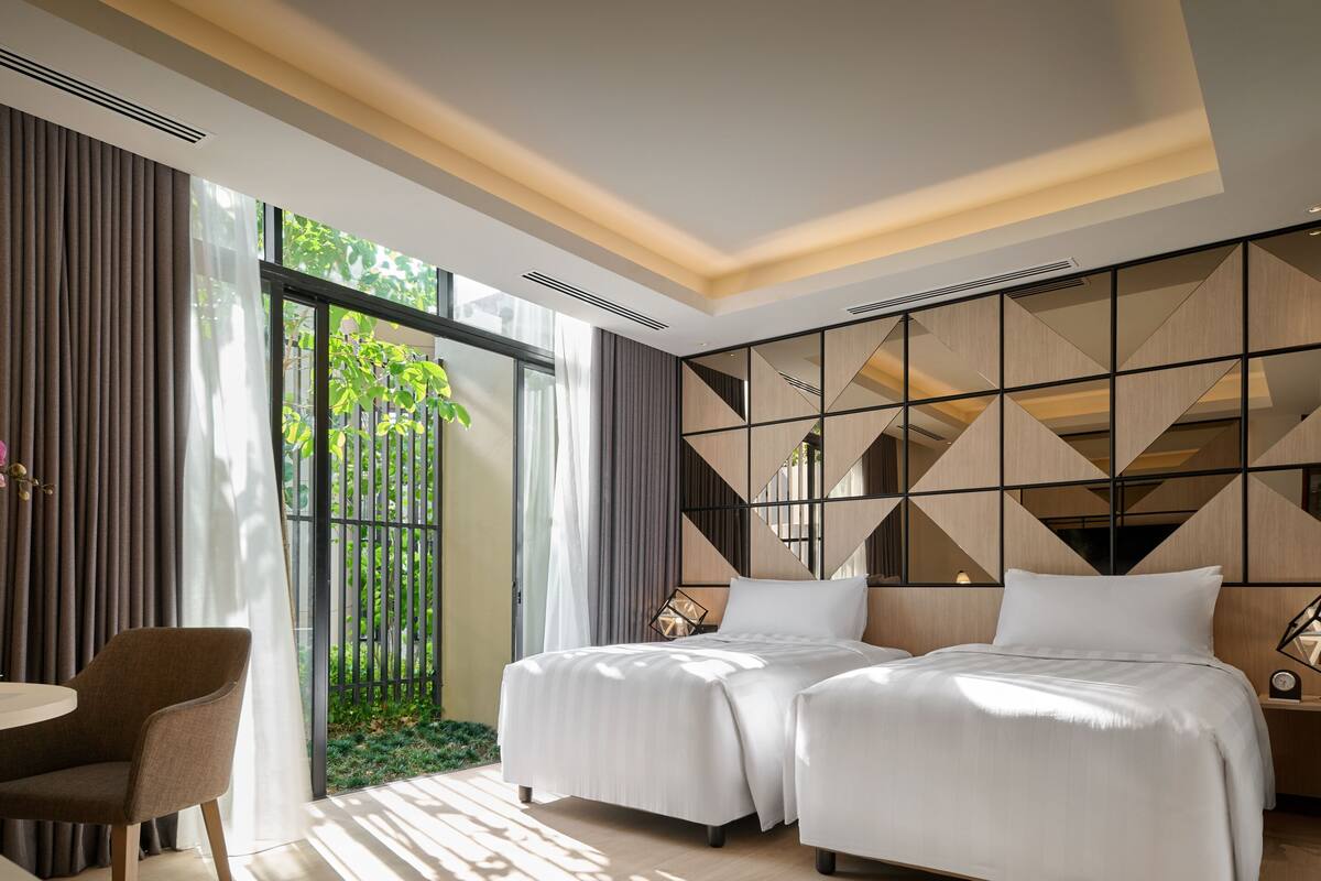 Une chambre d’hôtel avec deux lits, un bureau, une chaise et une grande fenêtre avec des rideaux.