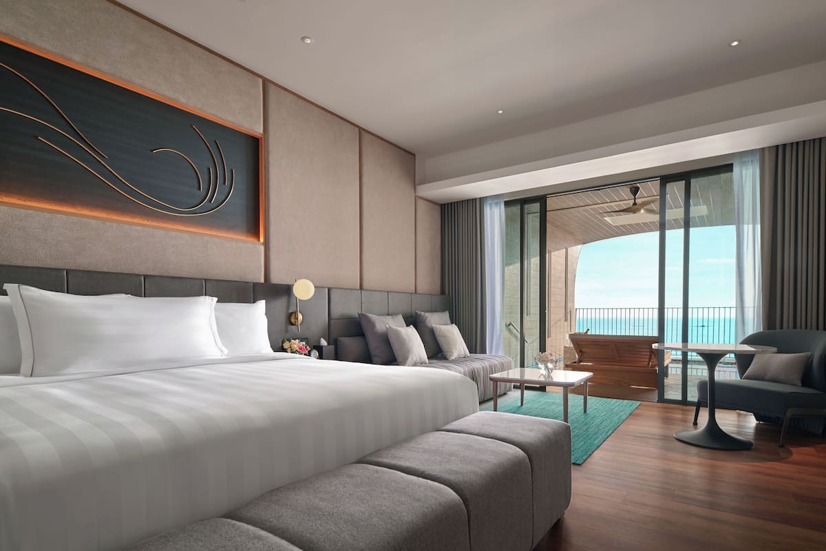 Une chambre d’hôtel moderne dotée d’un grand lit, d’un canapé, d’un coin repas et offrant une vue sur la mer.