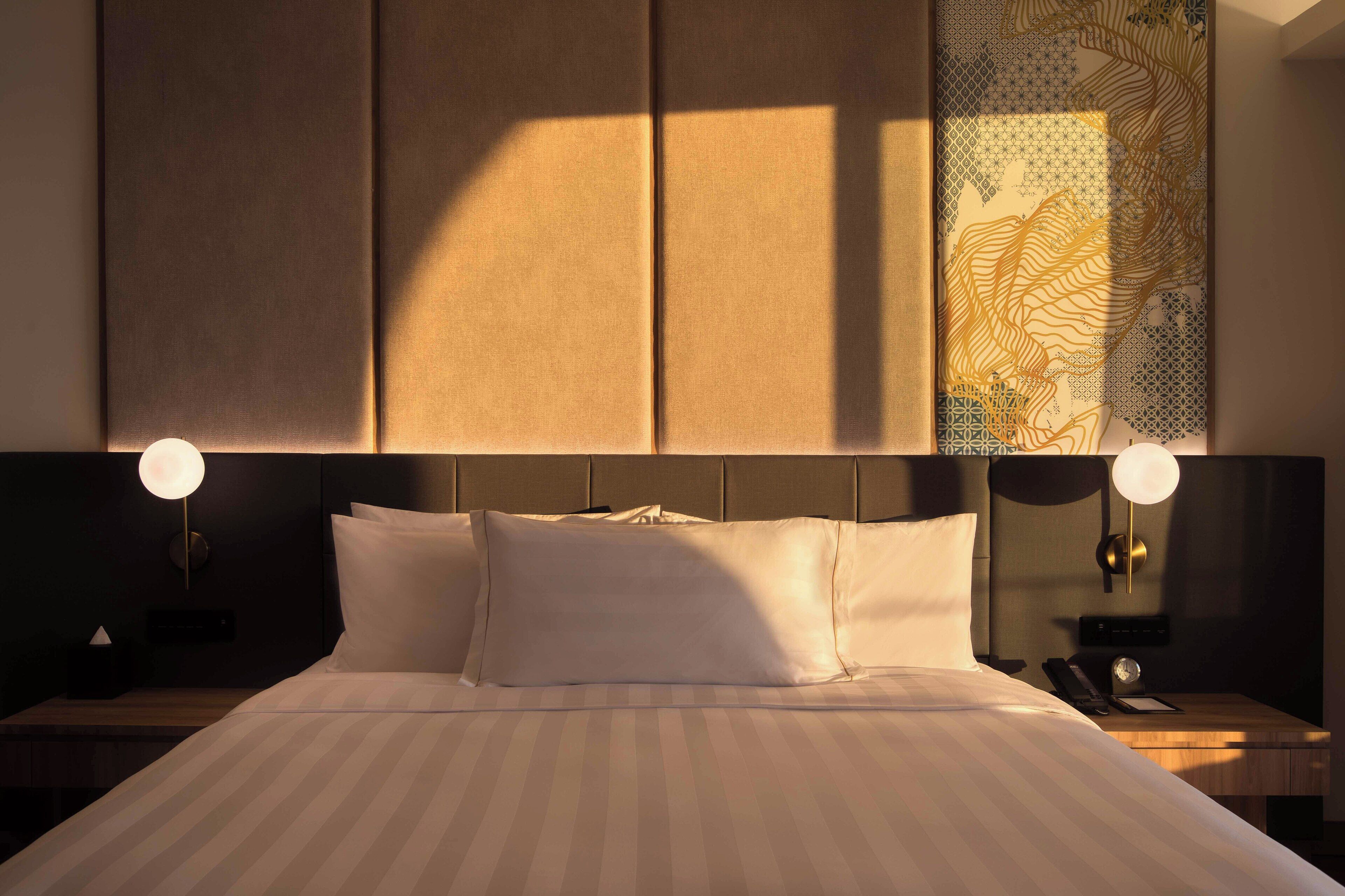 Ein Hotelzimmer mit einem großen Bett, zwei Nachttischen, einer Wandlampe und einem dekorativen Wandteppich.