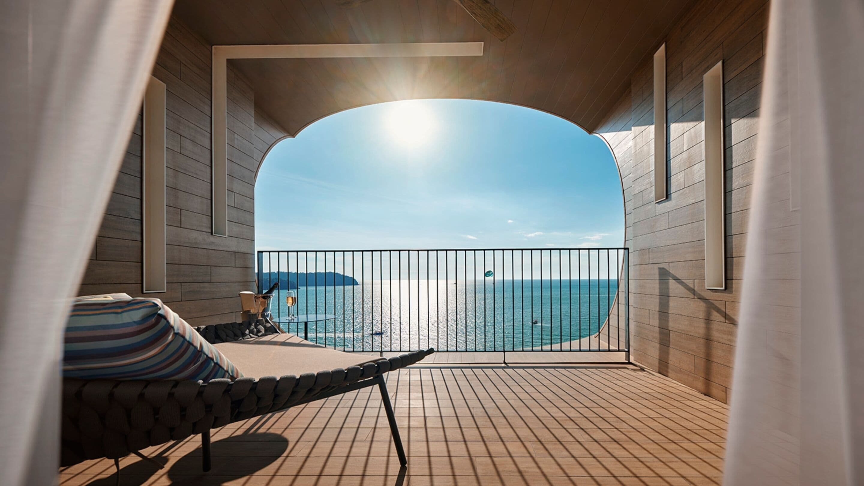 A balcony with a view of the sea, a chair, and a table with a glass of wine.