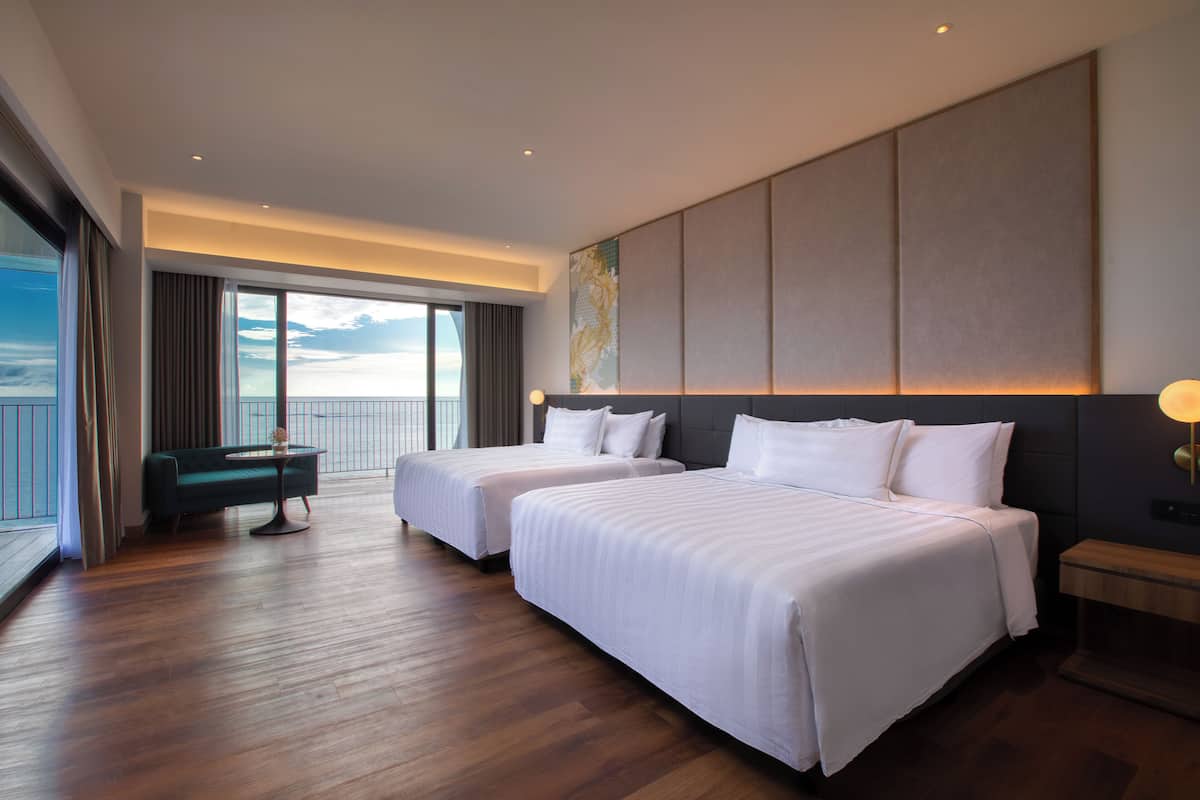 Une chambre d’hôtel avec deux lits, un coin salon et une grande fenêtre donnant sur un beau paysage.