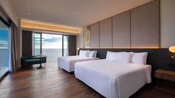 Habitación de hotel con dos camas, zona de estar y un amplio ventanal con vistas.